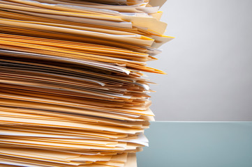 Tall pile of paperwork sitting on a clean office desk with wall of copy space