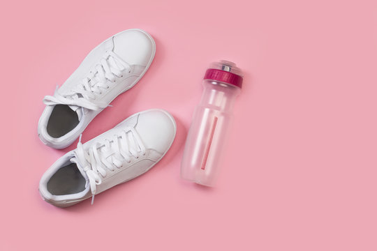 Zapatillas blancas junto a una botella de pl&aacute;stico sobre un fondo rosa liso y aislado. Vista superior. Copy space. Concepto: Fitness