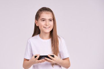 Naklejka premium Young pretty girl. Smiling studio portrait with smartphone. Female teenager typing sms to friend. Happy cute female kid