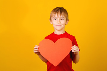 Cute smiling boy holding red paper heart. Child giving valentines heart. Love mood