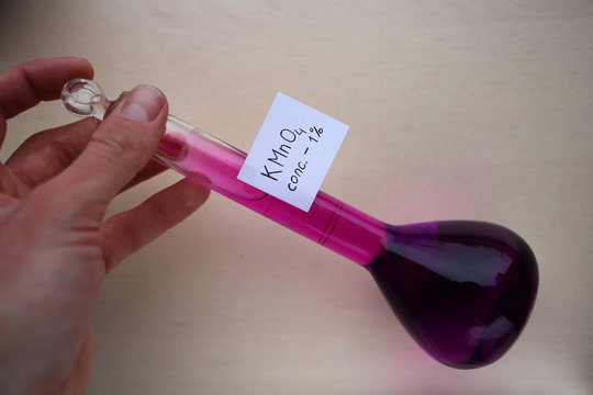 Mixing a purple aqueous solution of potassium permanganate in a flask by hand.
