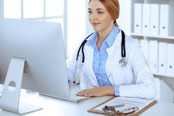 Young woman doctor at work in hospital looking at desktop pc monitor. Physician controls medication history records and exam results. Medicine and healthcare concept