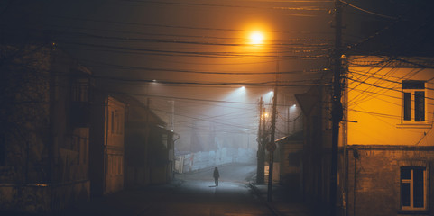 Lonely woman walking in foggy old city with street lights in a coat