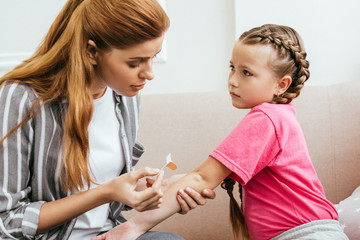 attractive mother applying adhesive bandage on elbow of daughter