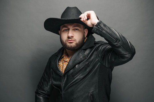 Cowboy studio portrait of a man wearing learher jacket and a hat with serious face