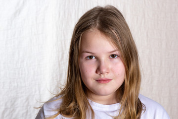 Portrait of blond beautiful girl 10 years old in front on light background, looking at camera,...