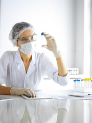 Naklejka premium Professional female scientist in protective eyeglasses researching tube with reagents in laboratory. Concepts of medicine and research
