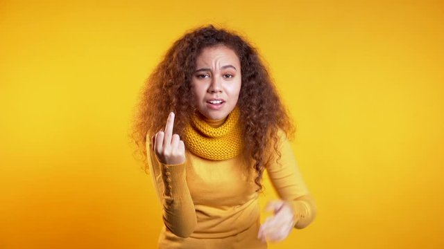Young pretty woman on yellow background showing middle finger - gesture of fuck. Expression negative, aggression, provocation.