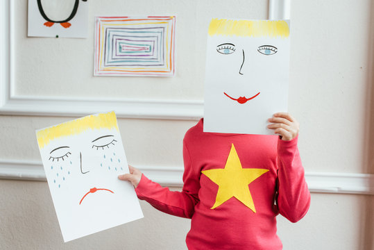 kid holding two paintings with happy and sad faces