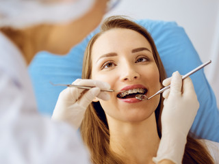 Smiling young woman with orthodontic brackets examined by dentist at dental clinic. Healthy teeth and medicine concept