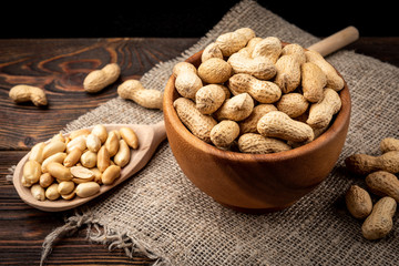 Peanut in the shell in wooden bowl on dark wooden background.