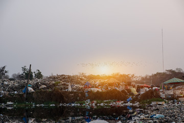 Polluted water and mountain large garbage pile and pollution at the sun is setting in the background
