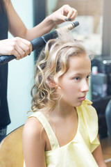 Fototapeta premium Hairdresser twists hair to blonde teen girl