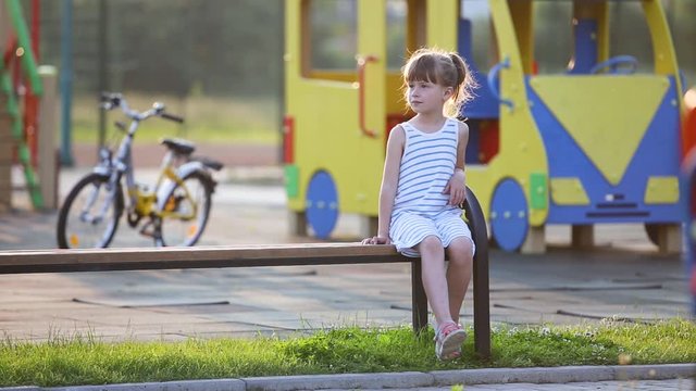 Cute little girl sitting on a bench and riding a bicycle on a school yard in summer.