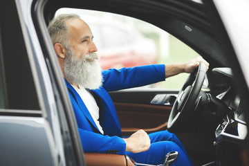 Old handsome man inside the car. Bearded mature male in the automobile. Confident businessman...