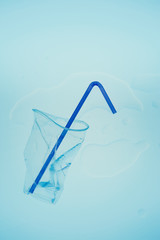 Squashed plastic cup and drink straw over blue background. Collecting plastic waste to recycling. Concept of plastic pollution and too many plastic waste. Copy space at the top