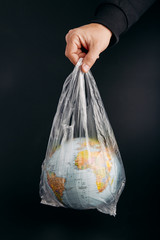 Male hand holding globe in a plastic bag. Earth contaminated by plastic waste. Concept of plastic pollution and plastic waste. Globe over black background. Copy space for text