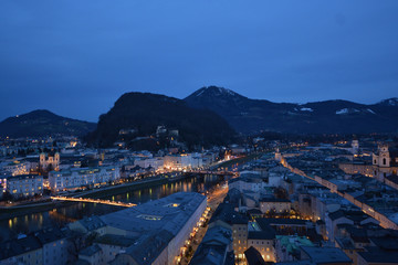 Salzburg evening cityscape with main Cathedral, Kollegienkirche and illuminated streets of old town on background of mountains in clouds