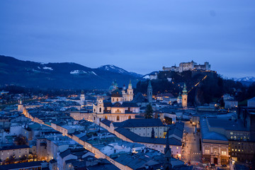 Salzburg evening cityscape with main Cathedral, Kollegienkirche and illuminated streets of old town on background of mountains in clouds