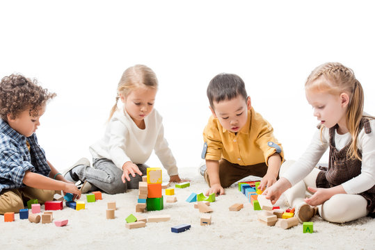 cute multiethnic children playing with wooden blocks on carpet, isolated on white
