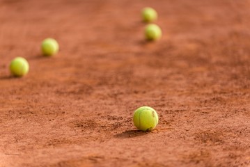 Tennis court covered in red sand and tennis balls under the sunlight with a blurry background