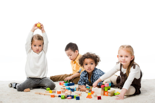 adorable multiethnic kids playing with wooden blocks on carpet, isolated on white