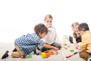 Obraz premium multicultural kids playing with wooden blocks on carpet, isolated on white