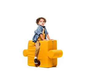 african american boy sitting on yellow puzzle chair, isolated on white