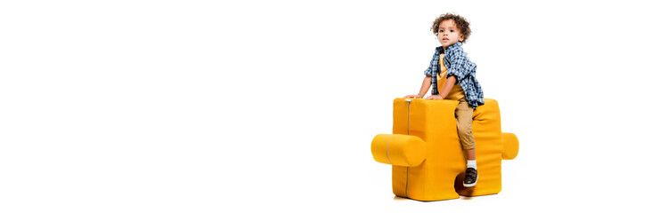 panoramic shot of little african american boy sitting on yellow puzzle chair, isolated on white