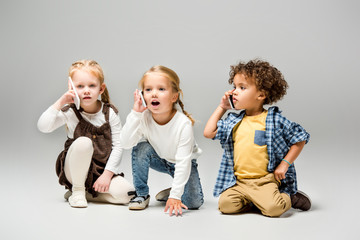 adorable multicultural kids talking smartphones on grey