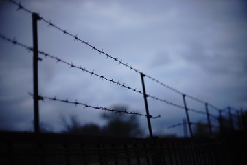 Damaged barbed wire fence in cloudy evening