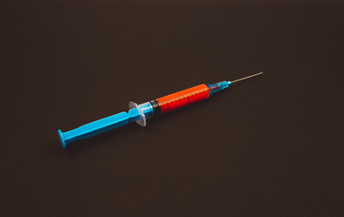 Blue syringe with a red vaccine against the epidemic of coronavirus on a black background