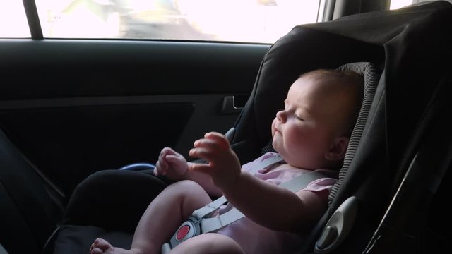 4K: Baby travelling in a Car seat in the back of a vehicle. This child is safely strapped in with a seatbelt on. 
