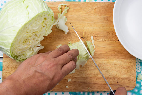 Chef cutting green cabbage on wooden broad