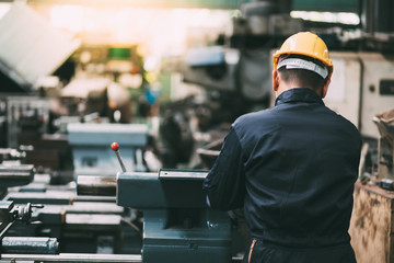 Factory Asian male worker. Asian man Lathe worker in production plant drilling at machine on the factory. Yellow hard hat safety first at mechanic factory.
