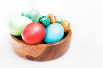 Fototapeta na wymiar Easter background. Bright multi-colored Easter eggs in a wooden plate on a white wooden surface, close-up