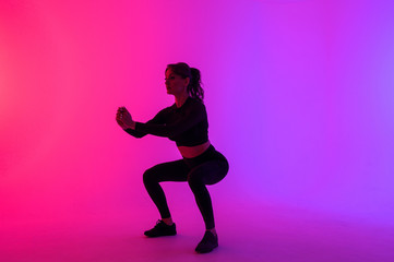 Fototapeta na wymiar Full length portrait of a young fitness woman doing squatting isolated on a vibrant colors background