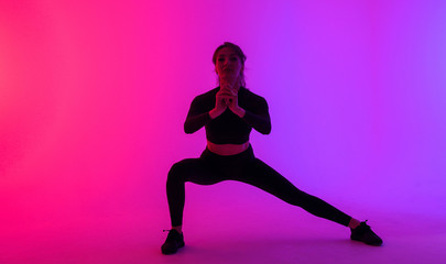 Fototapeta na wymiar Full length portrait of a young fitness woman doing squatting isolated on a vibrant colors background