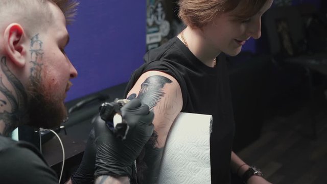 Footage of man doing tattoo of snake for woman in studio