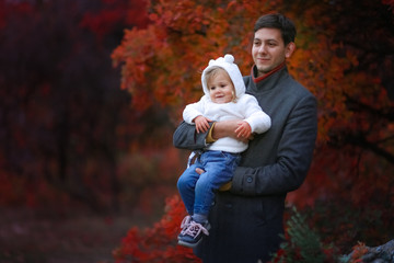 Fototapeta premium Father holds daughter, 2 years on hand in the sunshine trees in the background of brightly colored leaves.