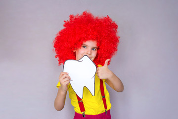 Little cute girl in a red clown wig with a toothbrush and a set of teeth in her hand. Concept of health, oral hygiene, people and beauty. Layout of the room. Selective focus.