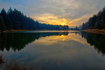 Fototapeta premium Meugliano lake is a moraine lake of the Ice Age, located in Meugliano, in Valchiusella, Piedmont, Italy. Seen at the sunset of a sunny winter day.