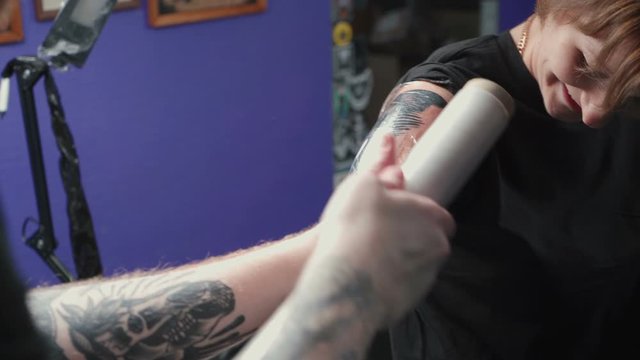 Footage of man doing dark tattoo of snake on woman in studio