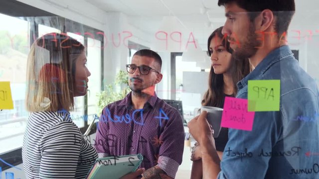 Video of successful business team discussing together in front of office glass board in the coworking space.