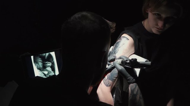 Footage of man doing dark tattoo of snake for woman