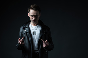 stylish brutal man in biker jacket showing middle fingers isolated on black