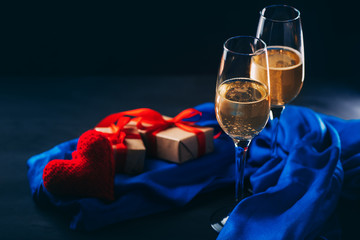 Glasses of champagne on a dark concrete table and a red heart with gifts. Celebrate Valentine's day copy space