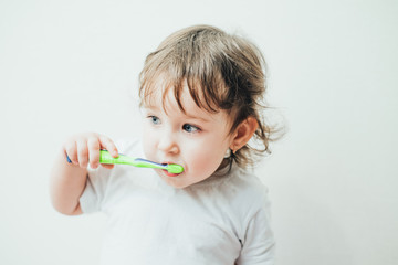 Little girl brushes her teeth with a toothbrush on a light background