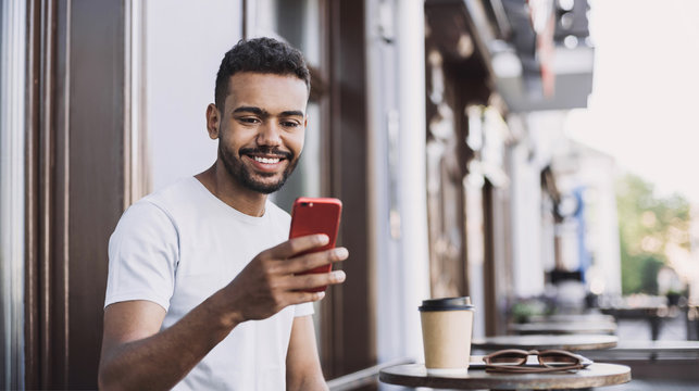 Handsome man using smartphone in a city. Young handsome student men having coffee break and texting on his mobile phone. Modern lifestyle, city life concept