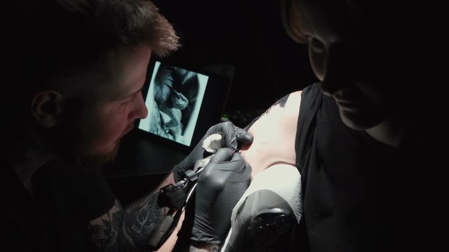 Footage of man doing black tattoo for woman in studio